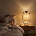 Reading in bed beside the black oval frame table lamp on a wood nightstand
