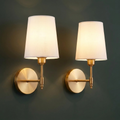 Fabric shade battery sconce in brushed brass on a deep charcoal green wall