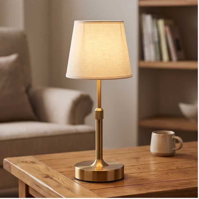 Gold cordless table lamp glowing on a wood side table beside a sofa