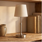 Silver cordless table lamp with neutral fabric shade on a wooden shelf