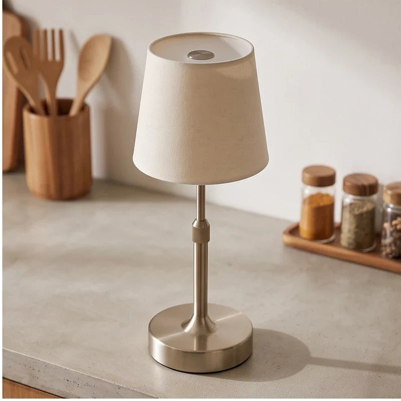 Silver cordless table lamp with off-white fabric shade on a light gray counter