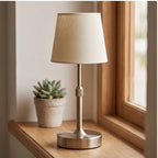 Gold cordless table lamp with cream fabric shade on a wooden window sill