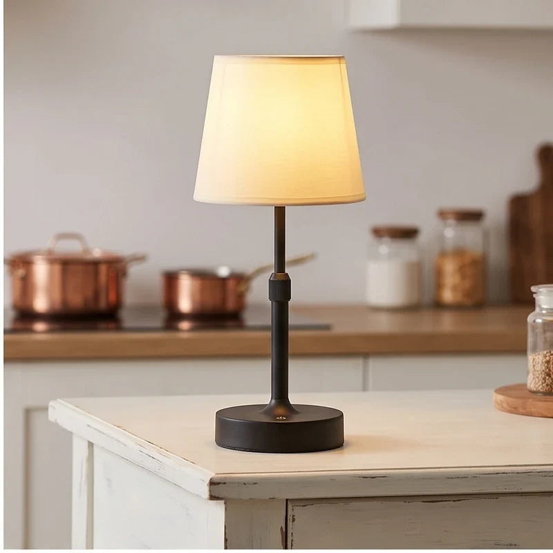 Black cordless table lamp with cream fabric shade on a white kitchen island